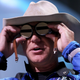 Amazon boss Jeff Bezos holding up watches to his eyes while wearing a cowboy hat at a space rocket launch.
